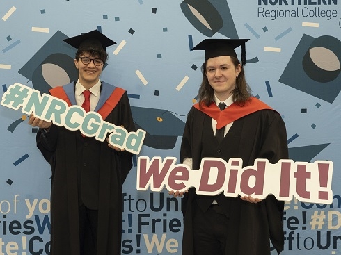 Two students in graduation robes holding props